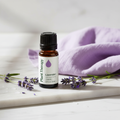 Lavender bottle on marble with fresh lavender sprigs and purple linen