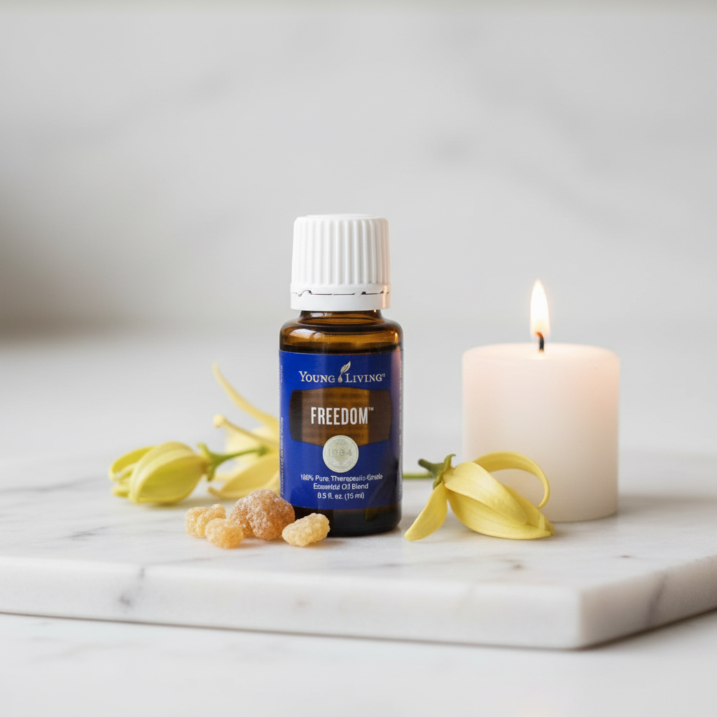 Young Living Freedom oil bottle on white marble with ylang ylang flowers and candle