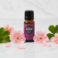 Edens Garden Rose Geranium Essential Oil on marble with pink geranium flowers and leaves